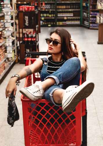 woman wearing blue jeans riding red shopping cart